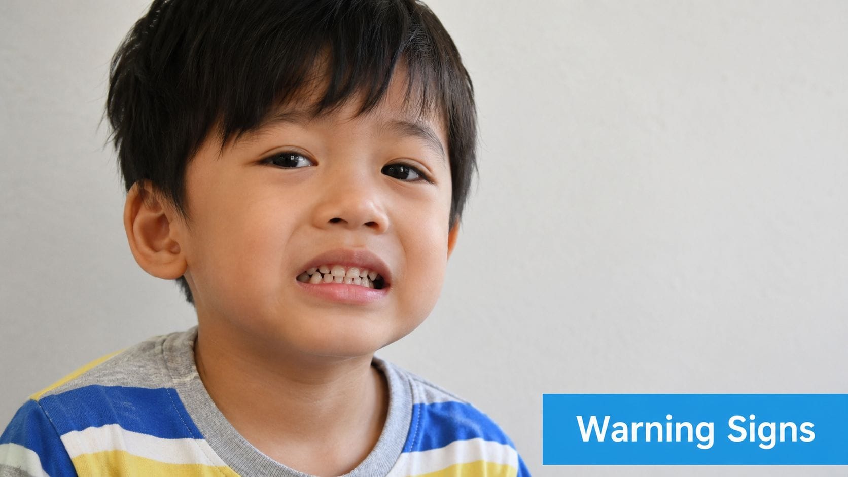 A close-up portrait of a young boy with an expressive face, possibly demonstrating signs of teeth grinding.
