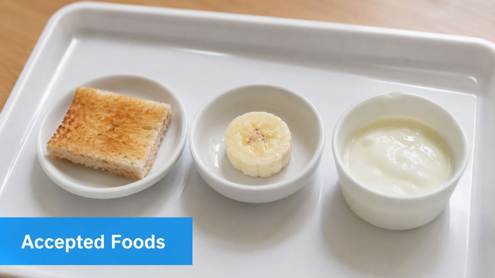 A white tray featuring three small bowls containing a piece of toast, a banana slice, and yogurt.