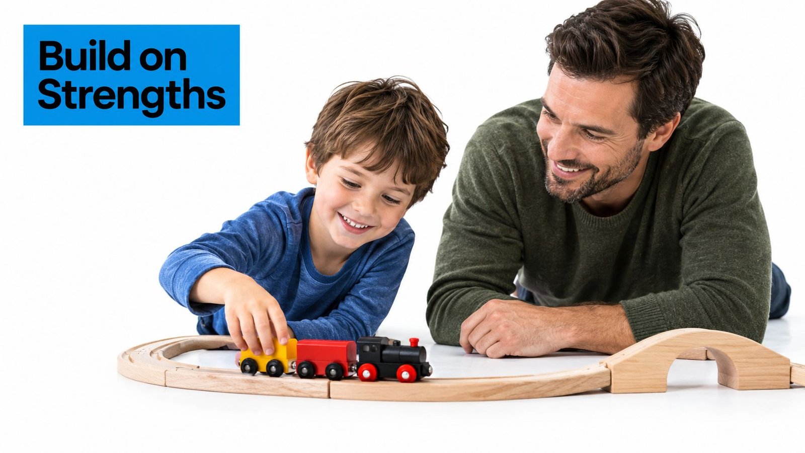 A smiling boy and his father play together with a wooden toy train on the floor.